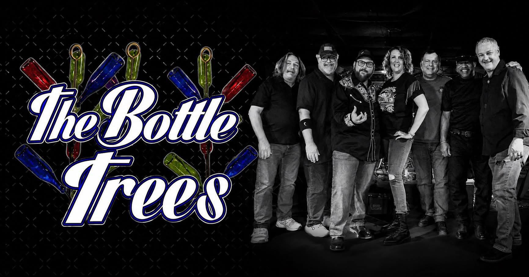 Group of eight people posing together on a dark stage beside a large neon-style logo reading The Bottle Trees with colorful bottle graphics on the left.